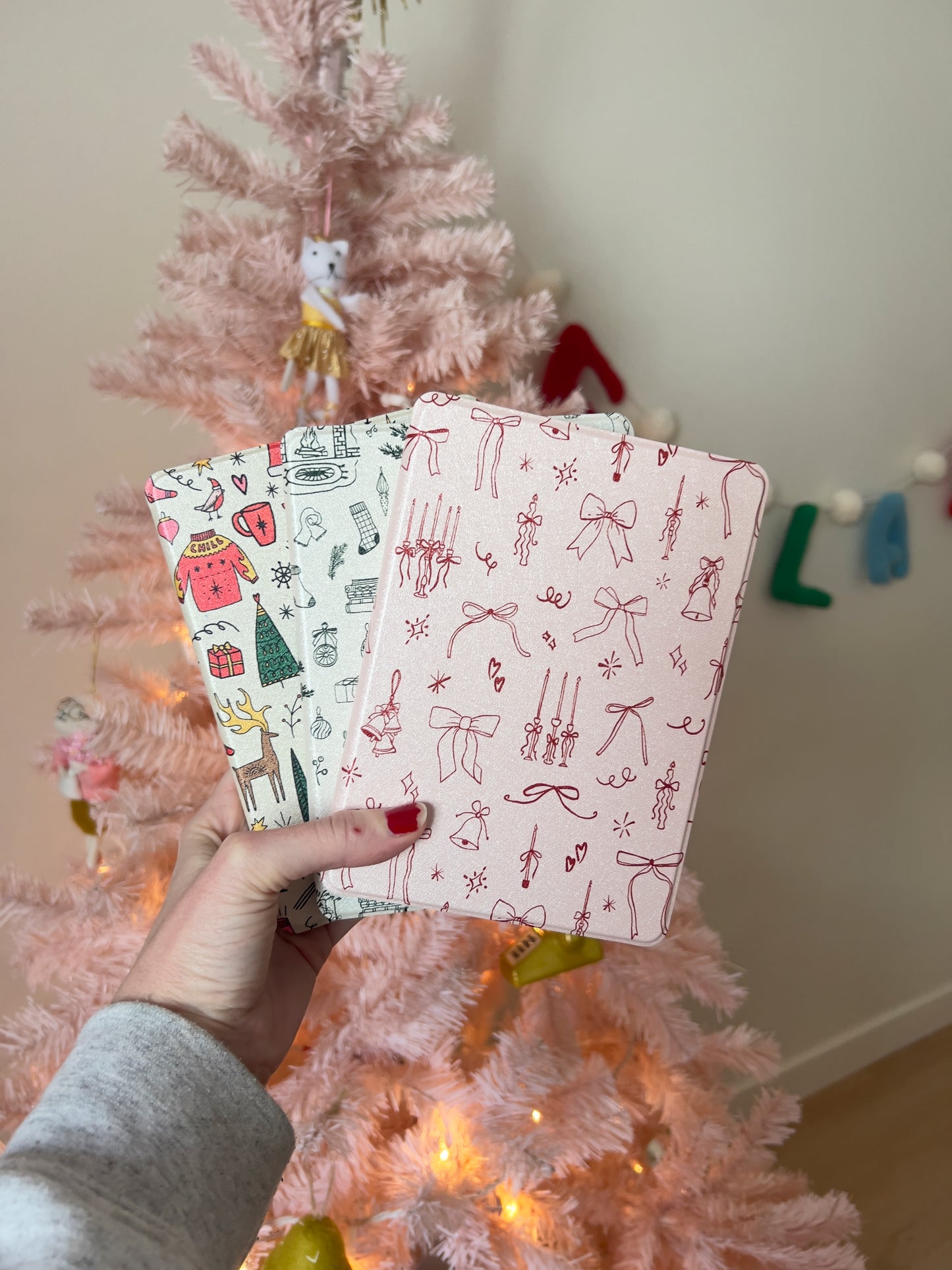 amazon kindle paperwhite case with a design of red bows, candles, and bells on a baby pink background.