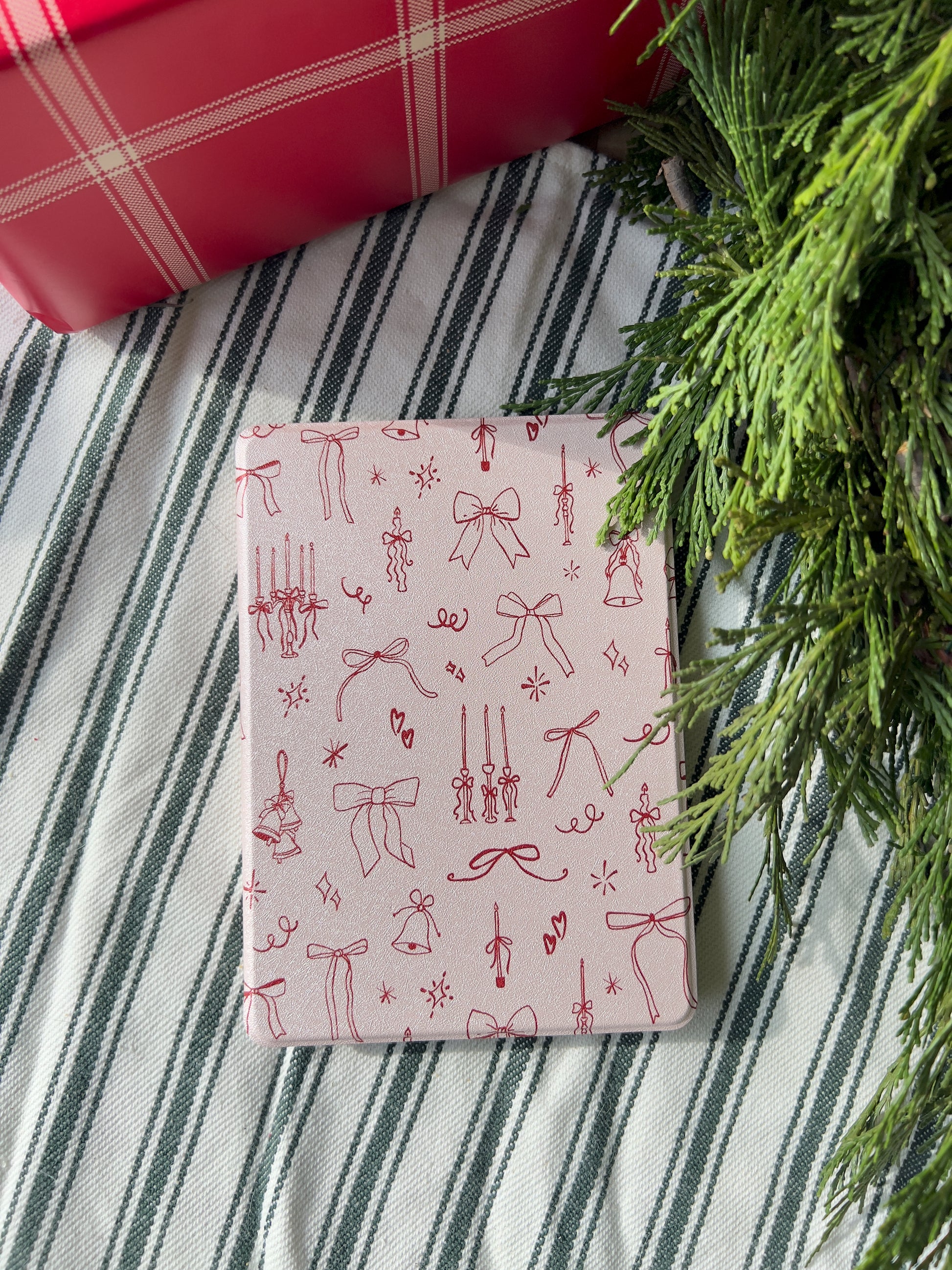 amazon kindle paperwhite case with a design of red bows, candles, and bells on a baby pink background.